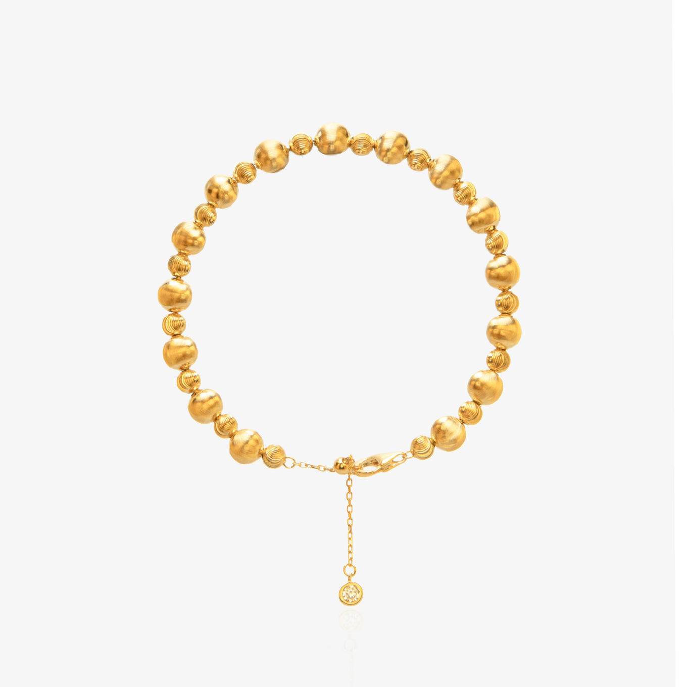Gold Bead Bracelet — alternating large smooth mirror-polished spheres and small threaded spiral spacer beads on elastic cord, with diamond-accented tag at lobster clasp extension, 18K gold plated, worn on wrist with white sleeve