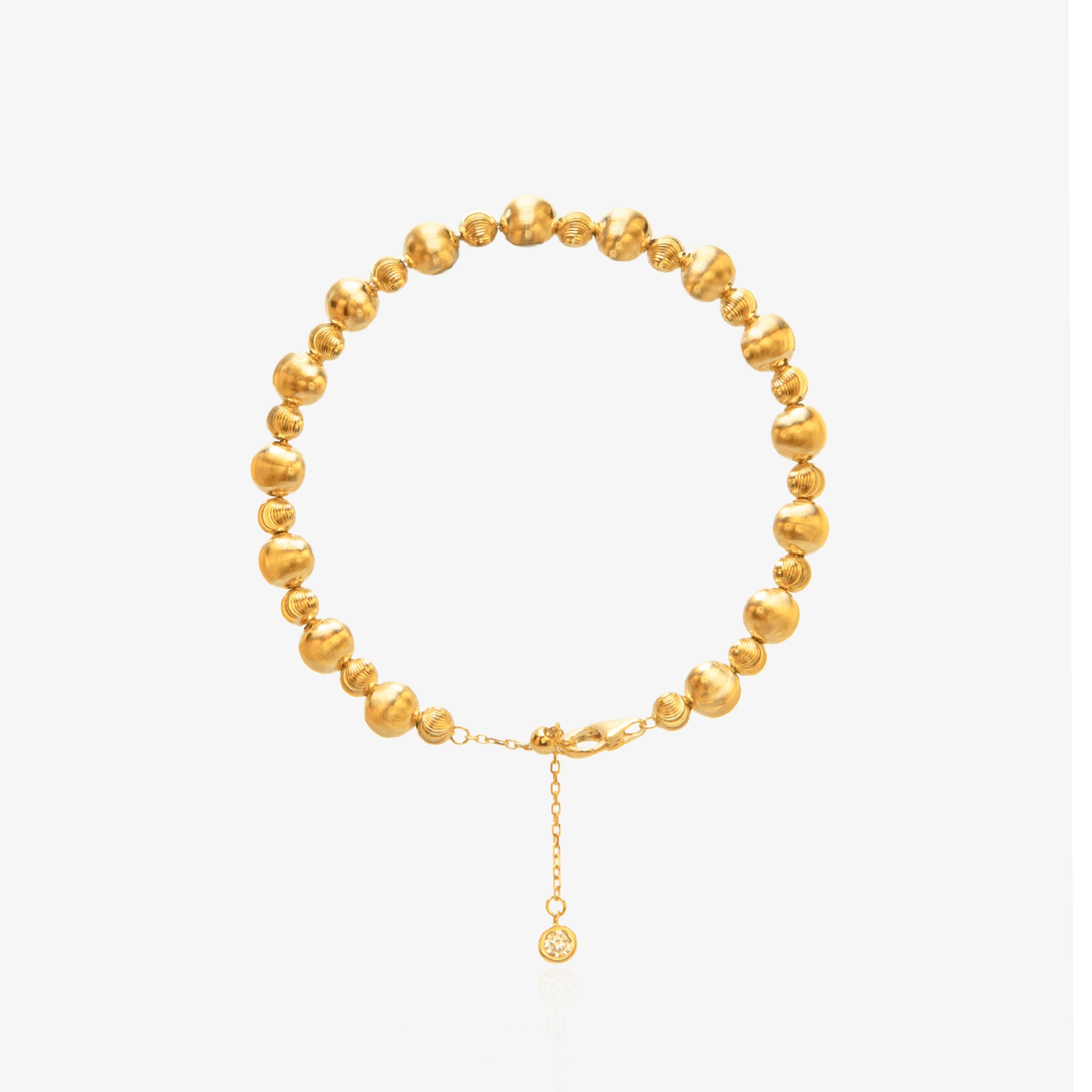 Gold Bead Bracelet — alternating large smooth mirror-polished spheres and small threaded spiral spacer beads on elastic cord, with diamond-accented tag at lobster clasp extension, 18K gold plated, worn on wrist with white sleeve