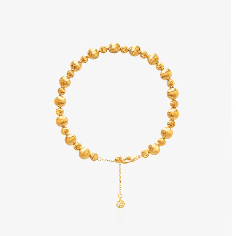 Gold Bead Bracelet — alternating large smooth mirror-polished spheres and small threaded spiral spacer beads on elastic cord, with diamond-accented tag at lobster clasp extension, 18K gold plated, worn on wrist with white sleeve