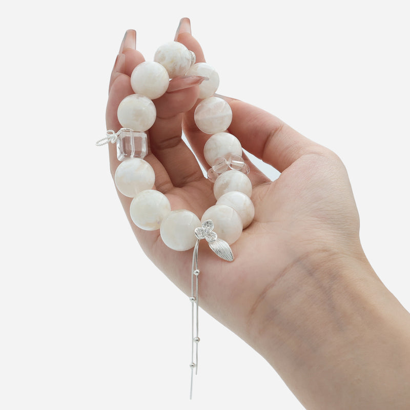 Close-up of hand holding creamy white phantom quartz bracelet showing the milky texture and 925 silver butterfly charm