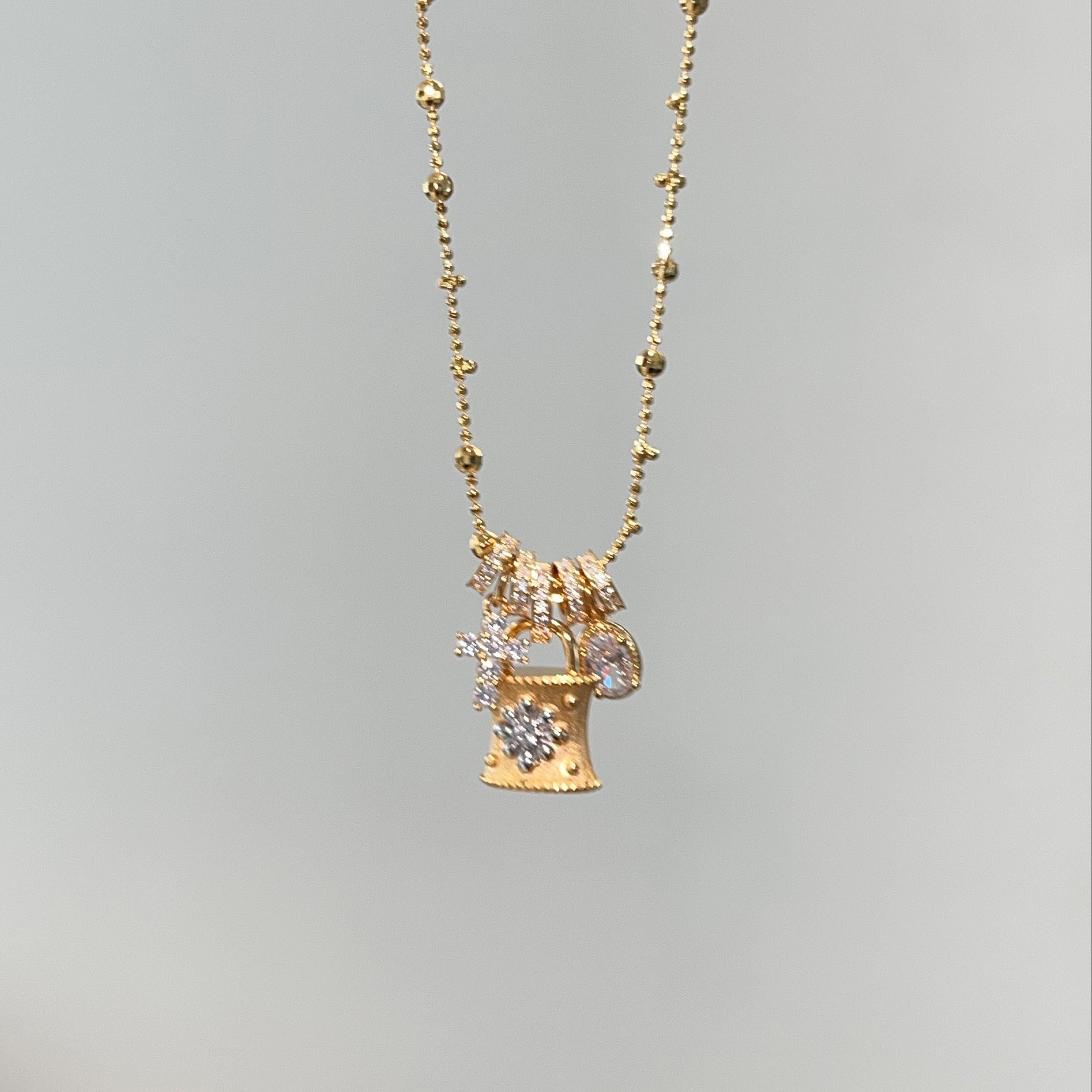 Gold Lock Charm Necklace worn on model — warm gold padlock with diamond snowflake center, detachable charms cascading naturally, beaded satellite chain at clavicle length, showing multi-pendant movement
