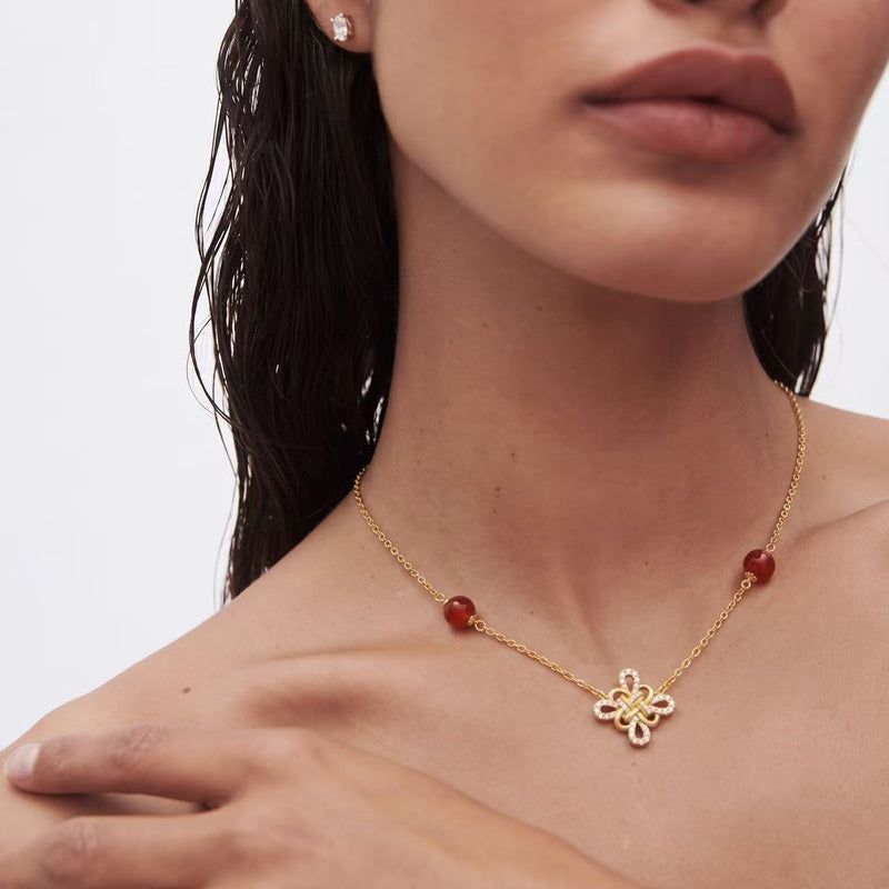 Gold Clover Necklace worn on model — four-petal knot pendant at clavicle length, red agate beads contrast against warm gold, pavé diamond border catching light, lightweight 5.22g, paired with natural styling