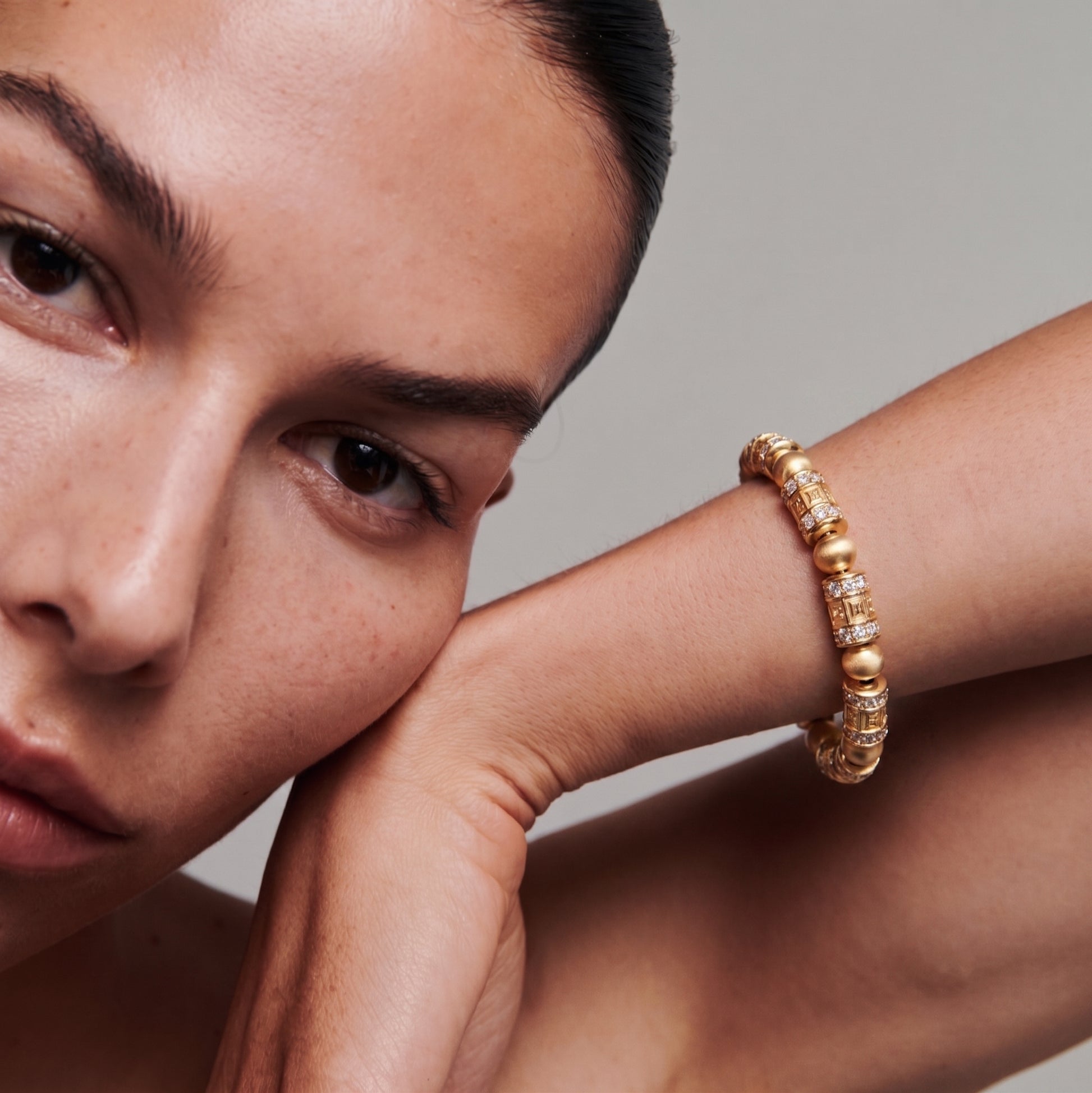 Close-up flat lay of mantra prayer wheel gold beaded bracelet — barrel-shaped beads with raised carved six-syllable mantra text and micro-claw diamond rings at both ends, alternating with smooth matte gold spacer spheres, elastic cord visible between beads