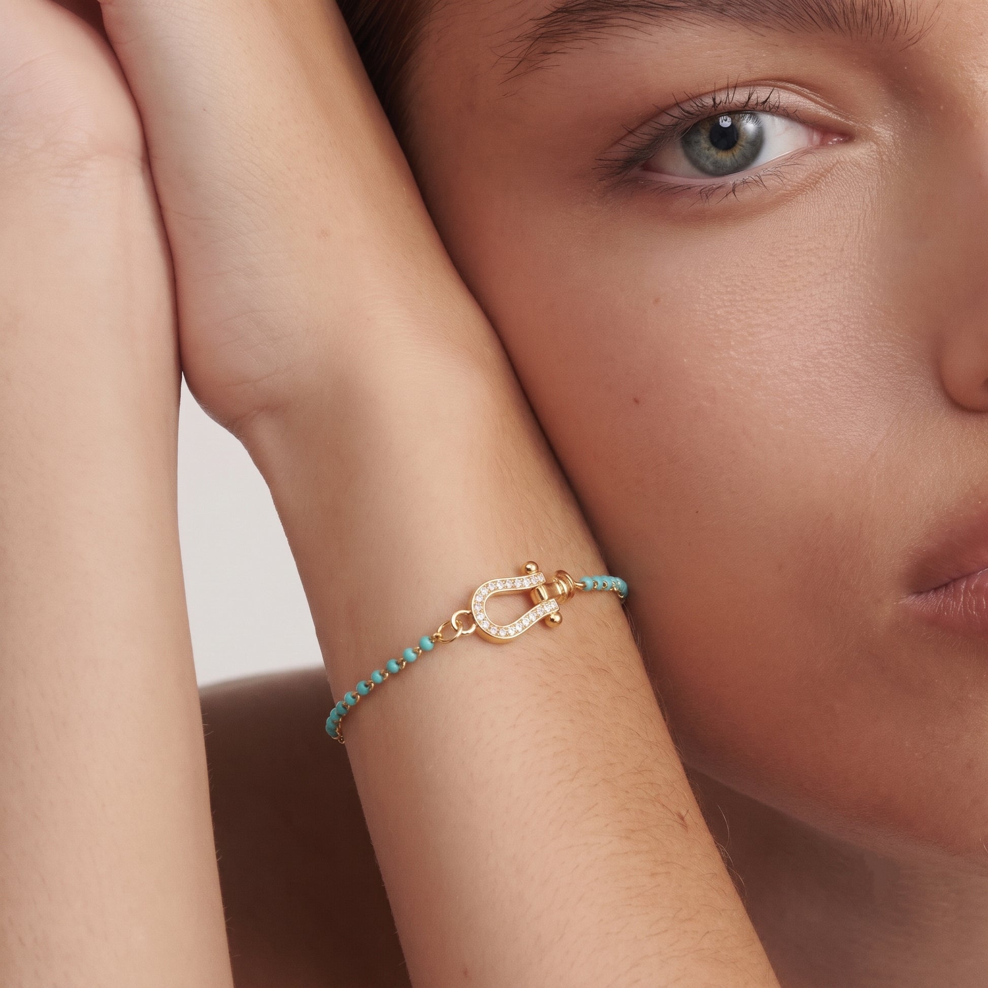 Close-up flat lay detail of two-tone bracelet — mint green cut beads, gold O-chain links, diamond-paved horseshoe clasp with rounded U-shape, lobster clasp and flat oval adjustment plate visible, satin-finished gold