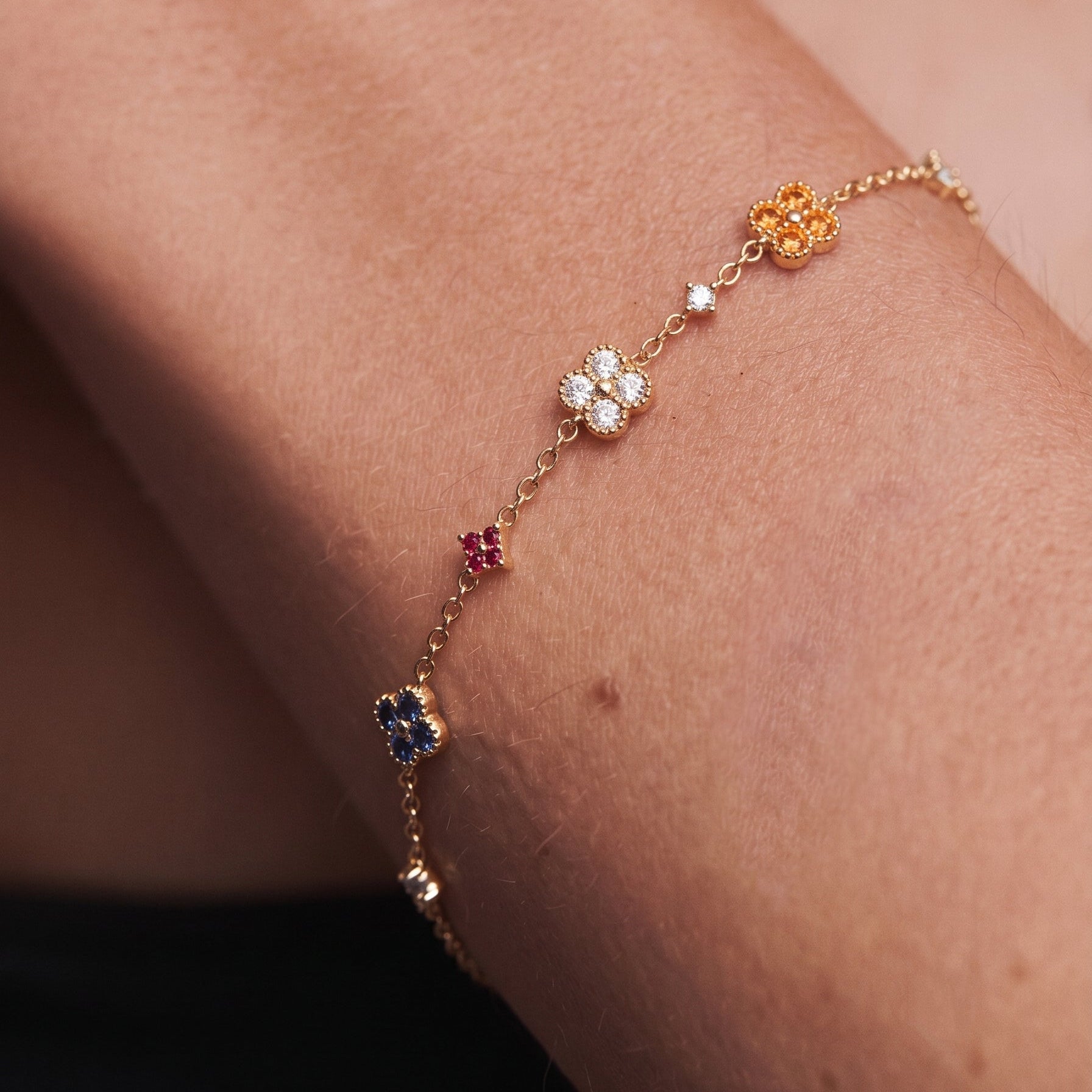 Multi-Color Clover Bracelet close-up detail — individual four-leaf clover charm with bezel-set colored stones and micro star accent on fine gold cable chain, showing pastel color contrast