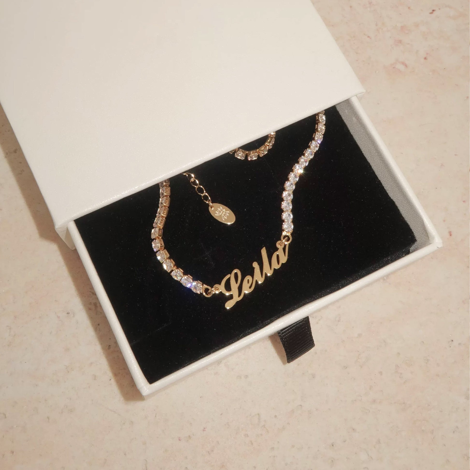Custom tennis name necklace detail — cursive script pendant on full-row CZ chain with continuous stone setting