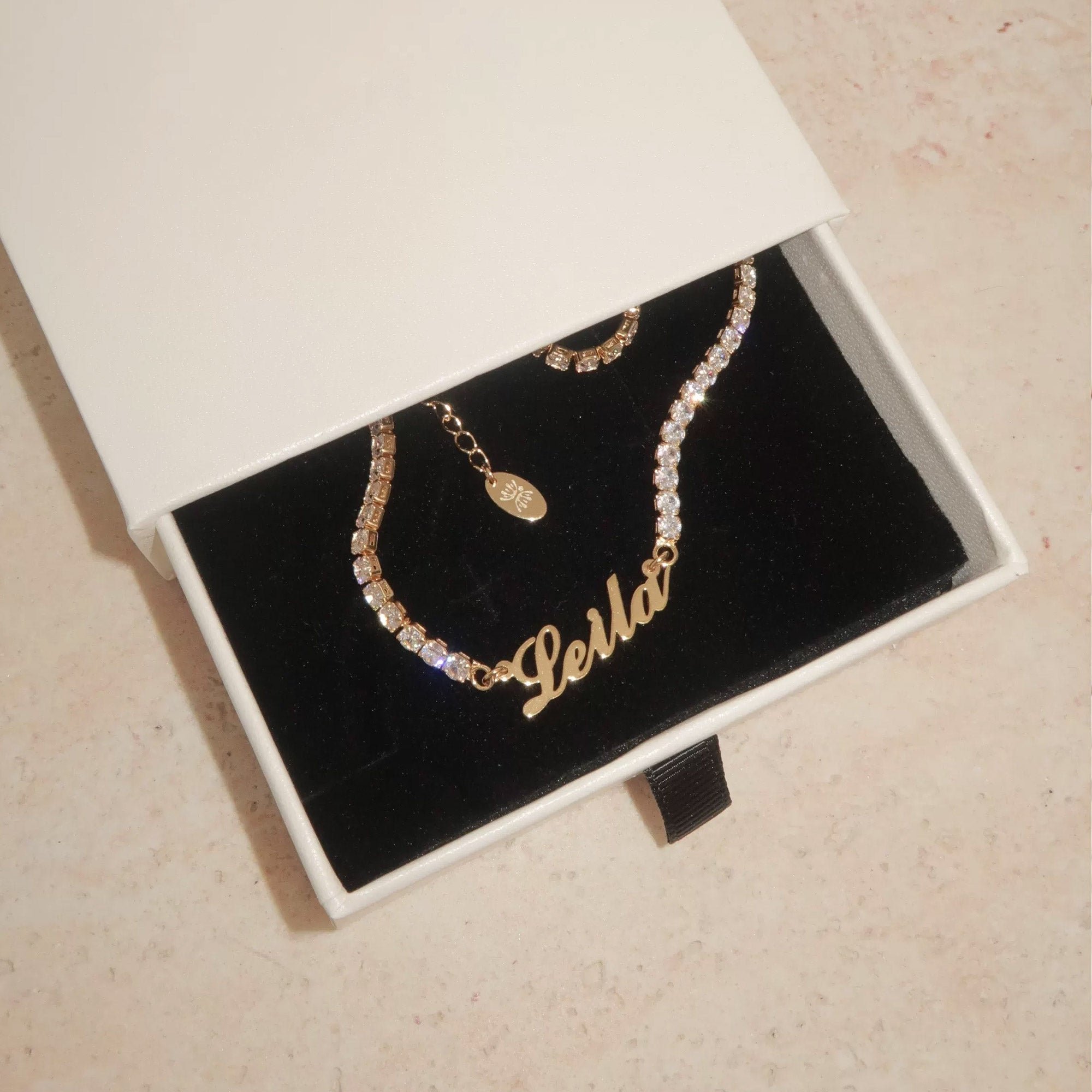 Custom tennis name necklace detail — cursive script pendant on full-row CZ chain with continuous stone setting
