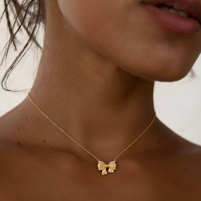 Gold ribbon bow necklace worn showing 3D satin texture with diamond accents French romantic style vintage-inspired everyday jewelry